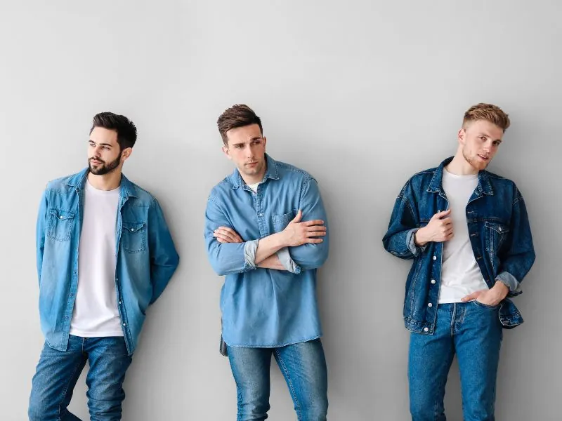 Quatro homens de jeans encostados em parede clara