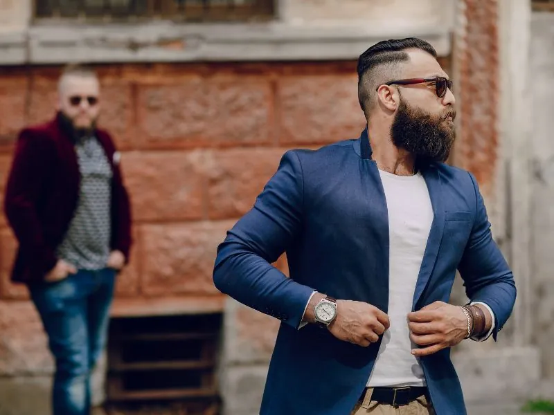 Homem de barba e blazer azul ajustando o paletó na rua