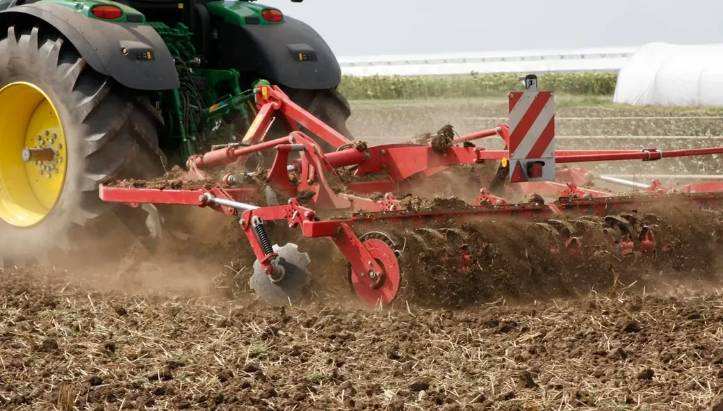 Trator arrastando implemento agrícola e levantando poeira no campo